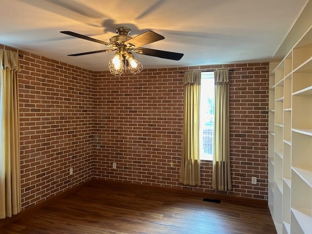 empty room featuring brick wall, dark wood-type flooring, and ceiling fan