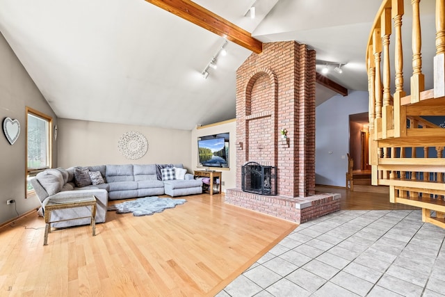 living room featuring light hardwood / wood-style flooring, lofted ceiling with beams, track lighting, and a fireplace