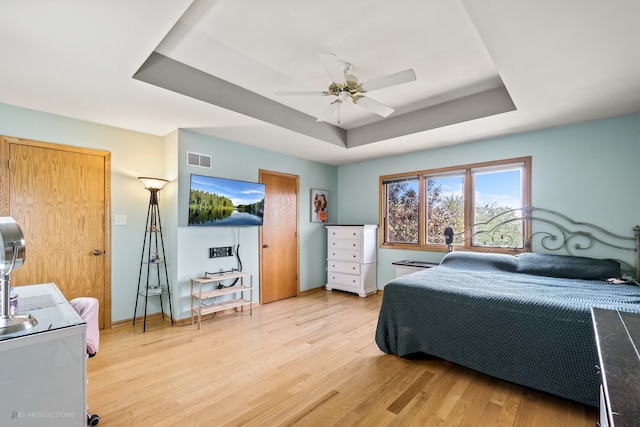 bedroom featuring ceiling fan, light wood-type flooring, and a raised ceiling