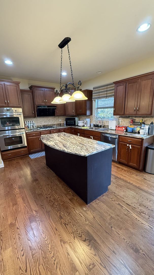 kitchen with light stone counters, appliances with stainless steel finishes, wood-type flooring, a center island, and decorative light fixtures