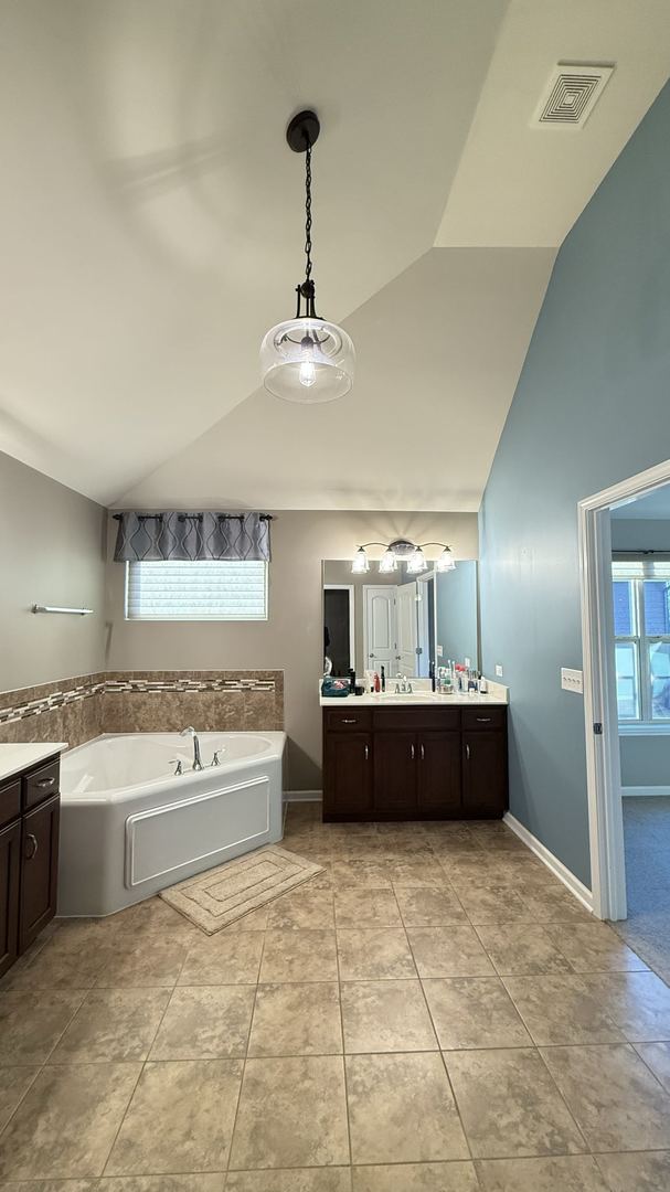 bathroom with vanity, a tub to relax in, tile patterned flooring, and vaulted ceiling