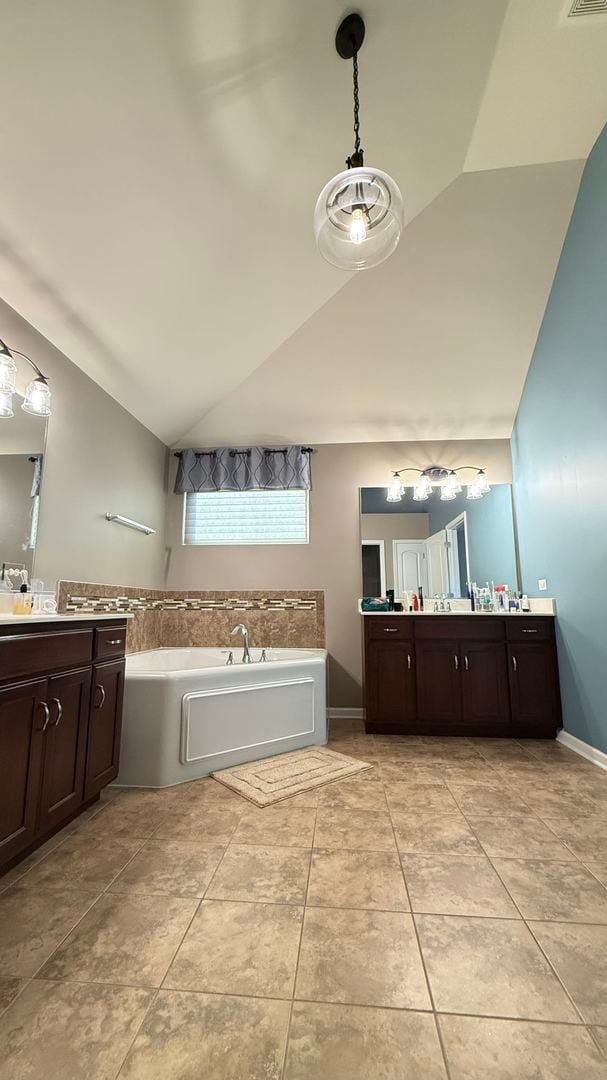 bathroom featuring vanity, vaulted ceiling, a tub to relax in, and tile patterned flooring