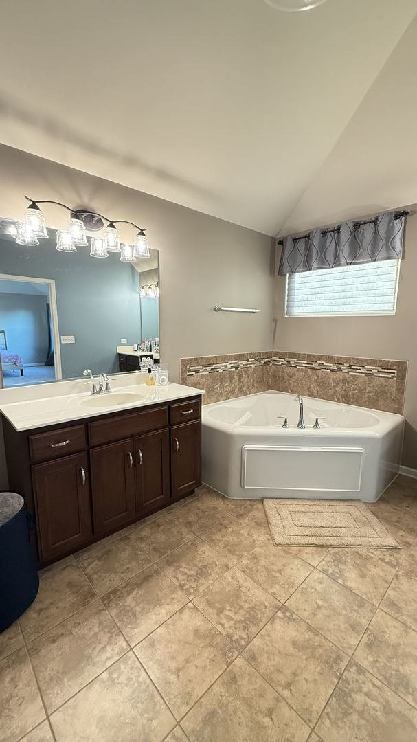 bathroom with vanity, lofted ceiling, a tub to relax in, and tile patterned floors