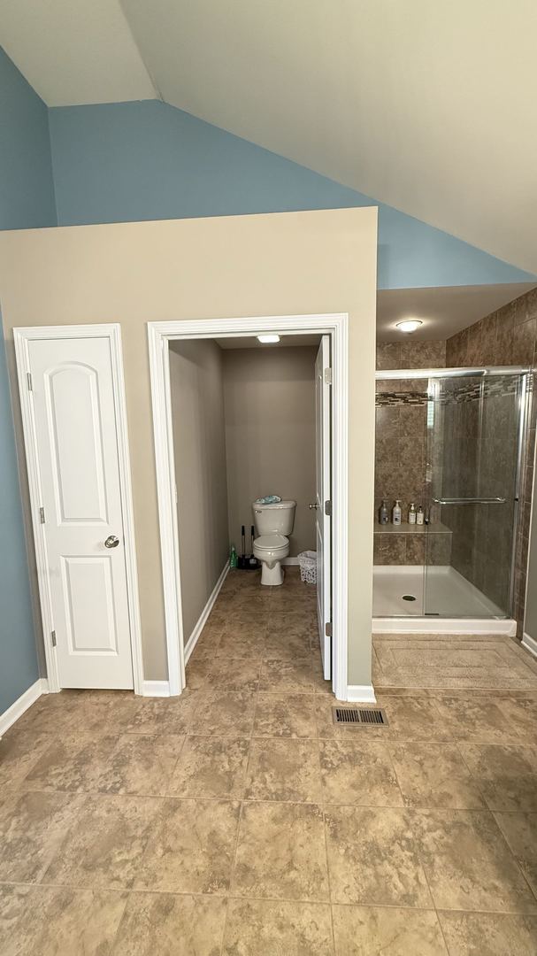 bathroom featuring lofted ceiling, a shower with shower door, and toilet