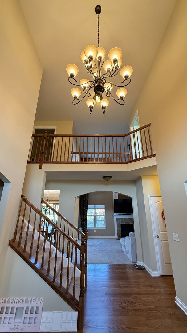 staircase featuring a notable chandelier, a fireplace, wood-type flooring, and high vaulted ceiling