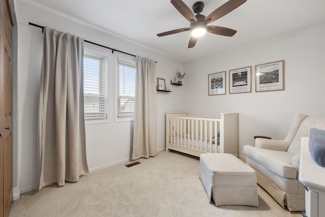 bedroom with ceiling fan, light colored carpet, and a crib