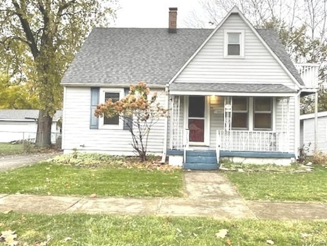 bungalow-style home with covered porch, a chimney, a shingled roof, and a front yard