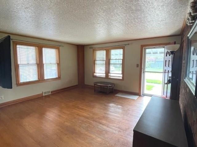 unfurnished living room featuring light wood-style floors, a textured ceiling, baseboards, and visible vents