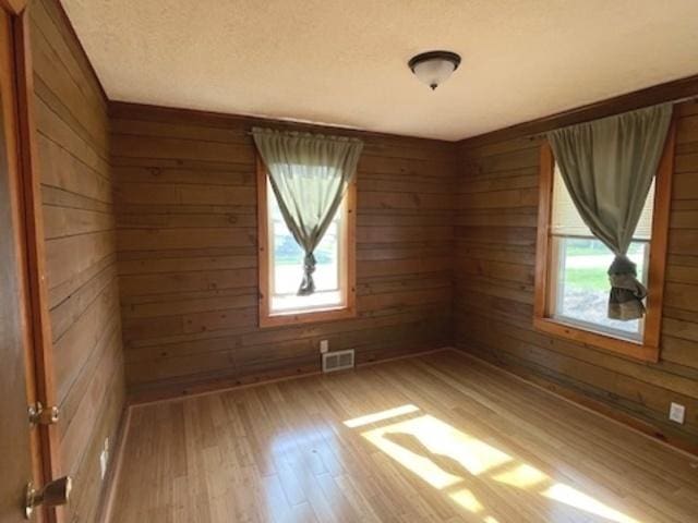 spare room featuring wooden walls, a wealth of natural light, light wood-type flooring, and visible vents