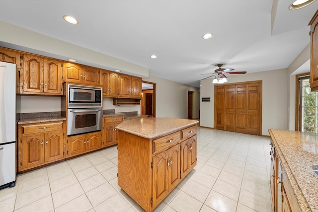 kitchen with light stone counters, appliances with stainless steel finishes, ceiling fan, light tile patterned floors, and a center island