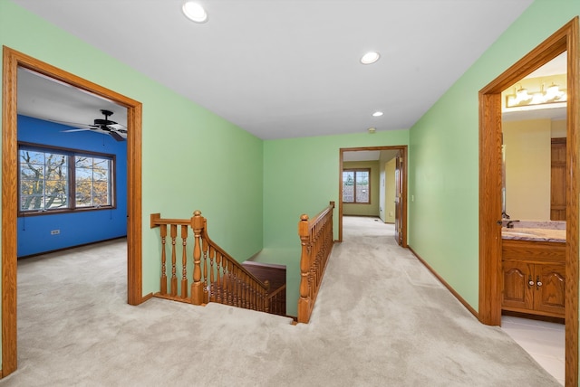 hallway with sink, light colored carpet, and plenty of natural light