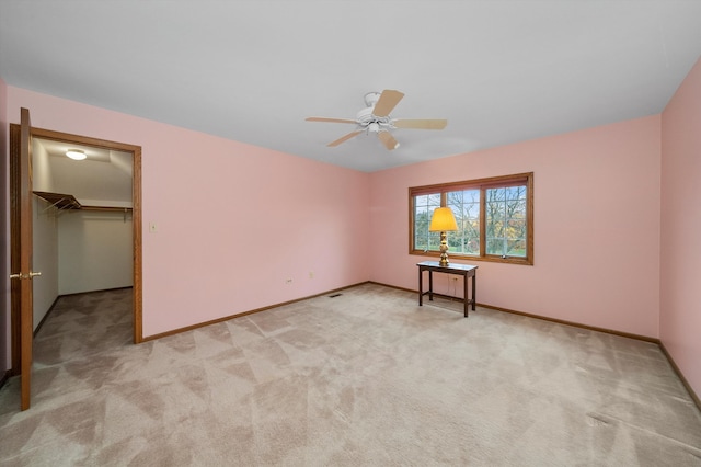 unfurnished bedroom with light carpet, ceiling fan, a walk in closet, and a closet