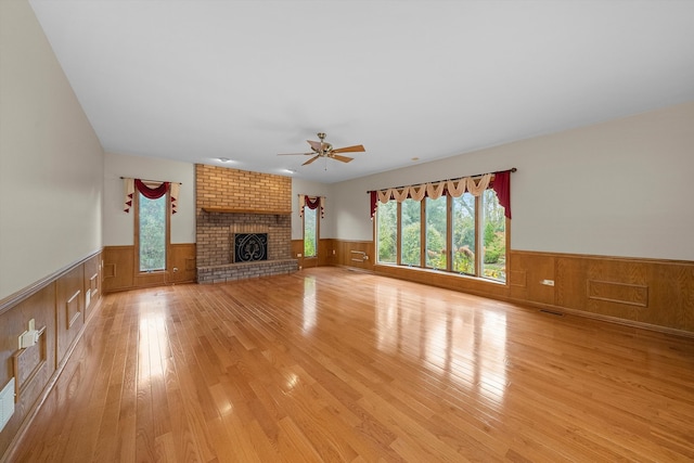 unfurnished living room featuring ceiling fan, a wealth of natural light, a brick fireplace, and light hardwood / wood-style flooring