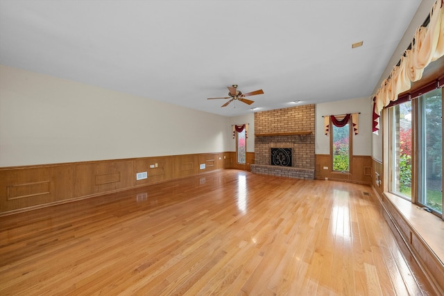 unfurnished living room with a brick fireplace, light hardwood / wood-style floors, ceiling fan, and wood walls