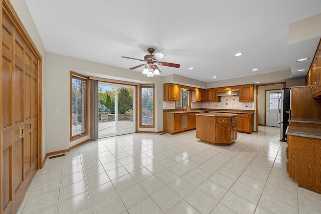 kitchen with light tile patterned floors, tasteful backsplash, a kitchen island, ventilation hood, and stainless steel fridge