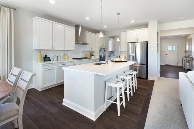 kitchen featuring dark hardwood / wood-style floors, wall chimney exhaust hood, stainless steel appliances, decorative light fixtures, and white cabinets