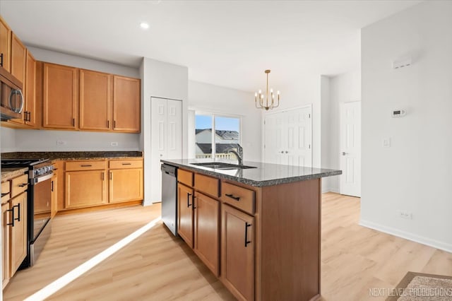 kitchen with an island with sink, appliances with stainless steel finishes, light hardwood / wood-style flooring, a notable chandelier, and sink