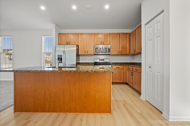 kitchen with a center island, stainless steel appliances, light hardwood / wood-style floors, and dark stone counters