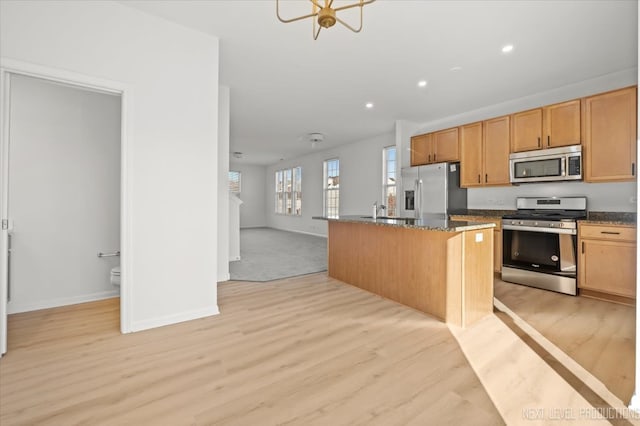 kitchen featuring appliances with stainless steel finishes, sink, light wood-type flooring, an island with sink, and dark stone countertops