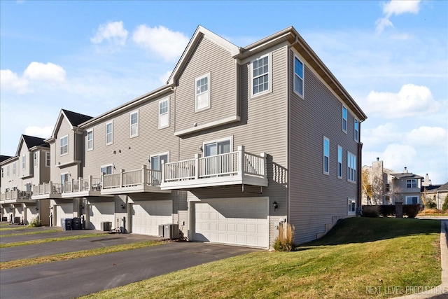 rear view of house with a yard, central AC, a balcony, and a garage