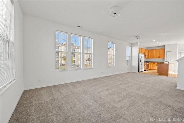 unfurnished living room featuring light carpet and a wealth of natural light