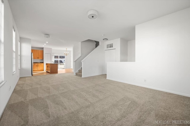 unfurnished living room featuring light carpet and a notable chandelier