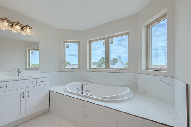 bathroom featuring vanity, a relaxing tiled tub, and a healthy amount of sunlight