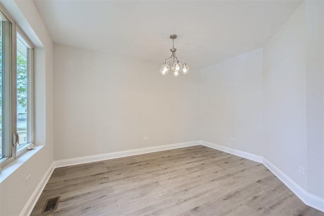 empty room with a wealth of natural light, a notable chandelier, and light hardwood / wood-style floors