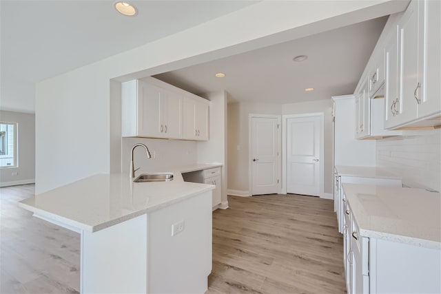 kitchen featuring kitchen peninsula, sink, white cabinets, light stone counters, and light hardwood / wood-style floors