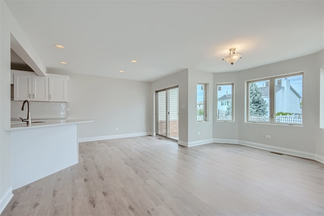 unfurnished living room featuring sink, light hardwood / wood-style floors, and a wealth of natural light