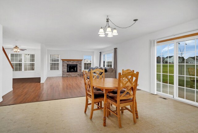 dining room with light wood-type flooring, a wealth of natural light, a fireplace, and ceiling fan with notable chandelier