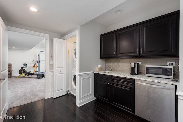 kitchen featuring dark wood-type flooring, sink, tasteful backsplash, light stone countertops, and stacked washer and dryer