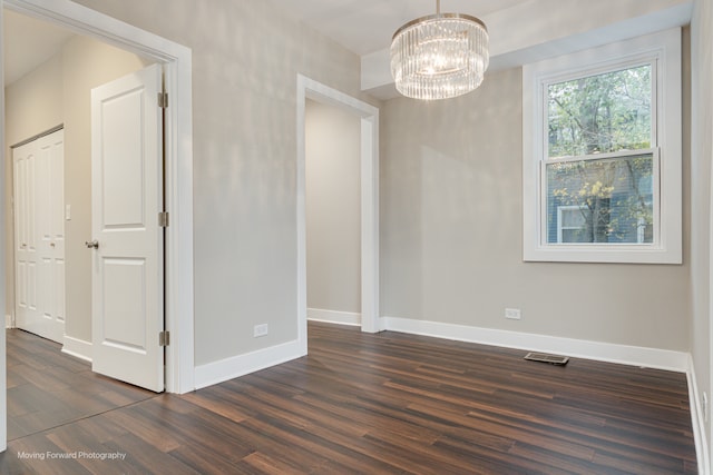 empty room with dark wood-type flooring and a chandelier