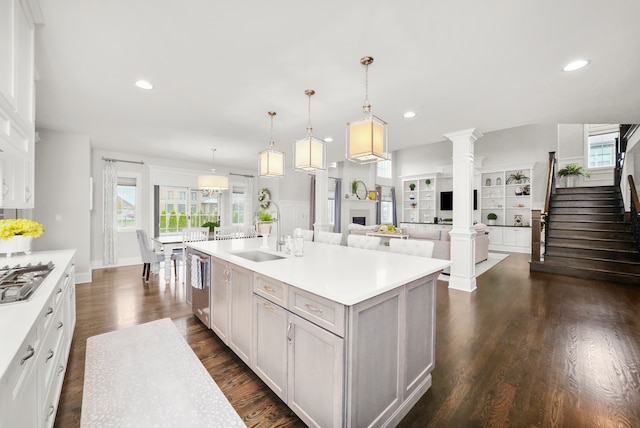 kitchen with sink, dark hardwood / wood-style flooring, decorative columns, decorative light fixtures, and a kitchen island with sink