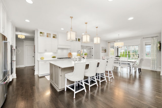 kitchen with backsplash, a kitchen island with sink, decorative light fixtures, dark hardwood / wood-style floors, and white cabinetry