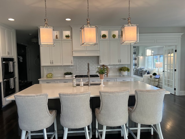 kitchen featuring a center island with sink, white cabinets, dark wood-type flooring, and decorative light fixtures