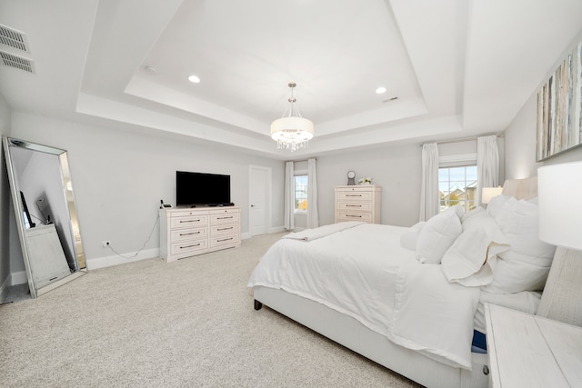 bedroom with light carpet, a tray ceiling, and a chandelier