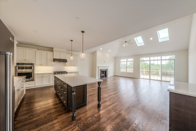 kitchen with dark wood-type flooring, white cabinets, hanging light fixtures, a kitchen island, and appliances with stainless steel finishes