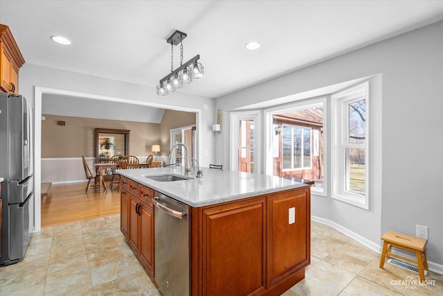 kitchen with light stone countertops, stainless steel appliances, sink, decorative light fixtures, and an island with sink