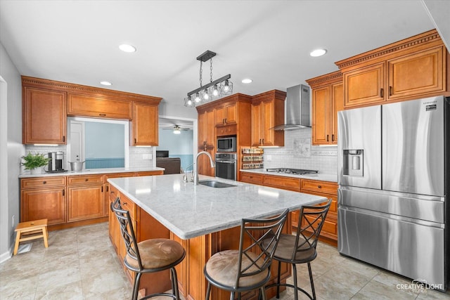 kitchen featuring a kitchen island with sink, sink, hanging light fixtures, wall chimney exhaust hood, and stainless steel appliances