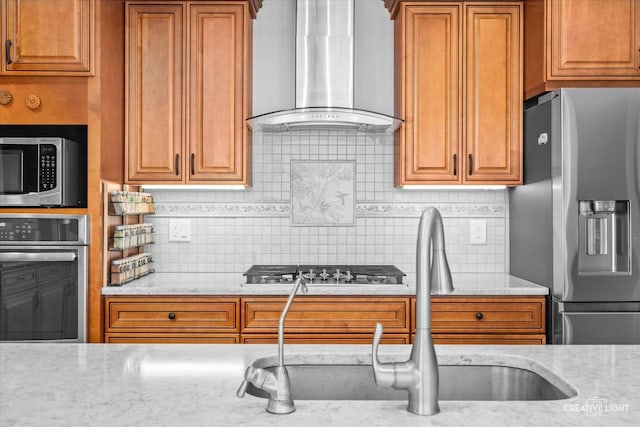 kitchen with wall chimney exhaust hood, light stone counters, appliances with stainless steel finishes, and tasteful backsplash