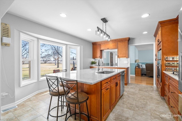 kitchen with light stone counters, stainless steel appliances, a kitchen island with sink, sink, and decorative light fixtures