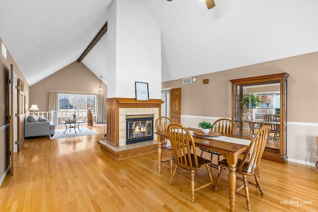 dining area with a tile fireplace, ceiling fan, light hardwood / wood-style floors, and vaulted ceiling with beams