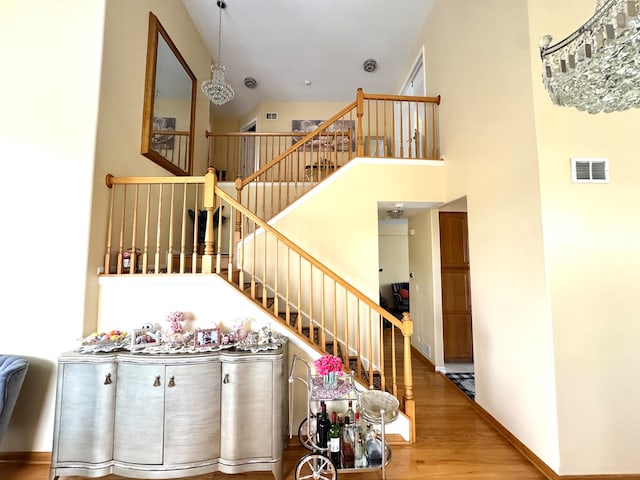 staircase with hardwood / wood-style floors, a towering ceiling, and a notable chandelier