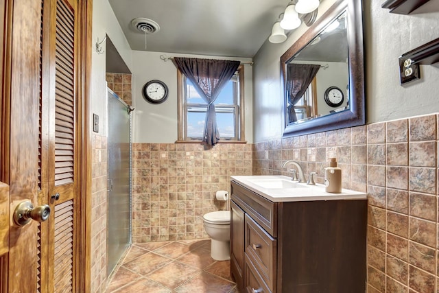 bathroom with a shower with shower door, tile walls, tile patterned flooring, vanity, and toilet