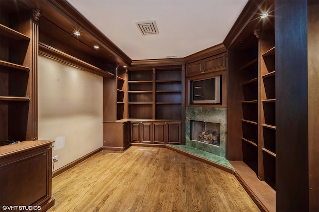 interior space featuring crown molding, built in shelves, a fireplace, and light hardwood / wood-style flooring