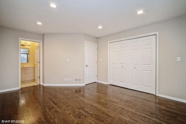 unfurnished bedroom featuring dark wood-type flooring, ensuite bathroom, and a closet