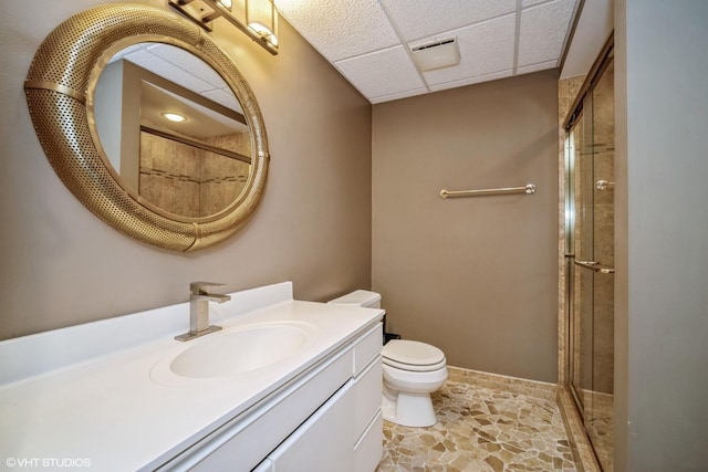 bathroom with toilet, a shower with door, and a drop ceiling