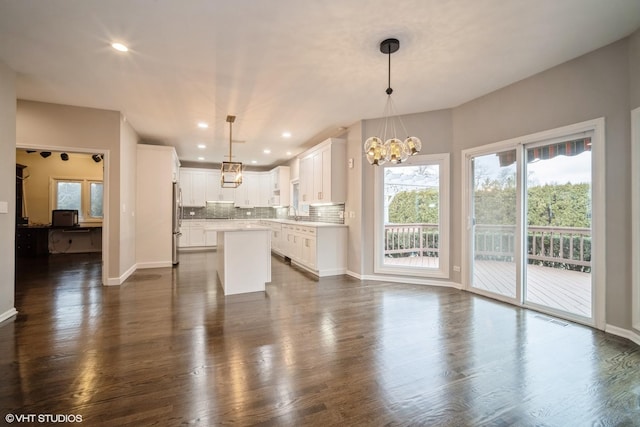 kitchen featuring decorative light fixtures, stainless steel fridge, white cabinets, and a kitchen island