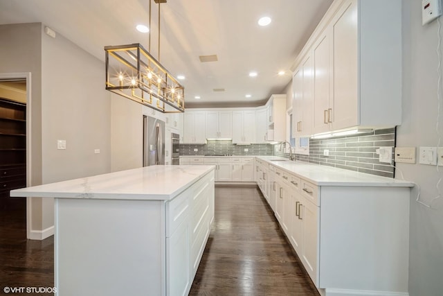 kitchen with white cabinetry, light stone countertops, a center island, and pendant lighting